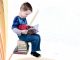 Na zdjęciu chłopiec z ksiązką siedzący na stosie książek