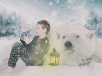 Na zdjęciu w zimowej scenerii czytający książkę chłopiec z białym niedźwiedziem.