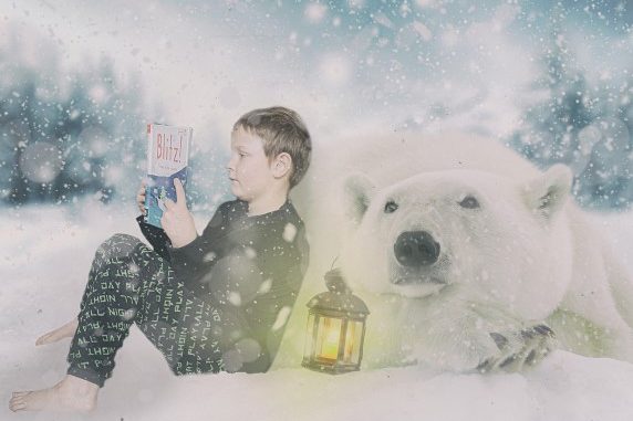 Na zdjęciu w zimowej scenerii czytający książkę chłopiec z białym niedźwiedziem.