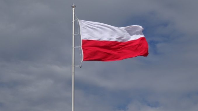 Na tle niebieskiego nieba powiewająca na maszcie biało czerowna flaga Polski