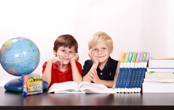 Biurko z książkami i globusem, a za nim dwóch siedzących chłopców z rękami podpierajacymi brody