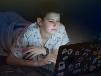 Na zdjęciu dziecko leżące w łóżku nocą przed komputerem.