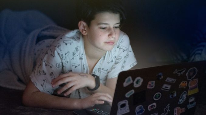 Na zdjęciu dziecko leżące w łóżku nocą przed komputerem.